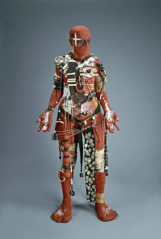 A reddish clay body strung with strings, necklaces, photographs of faces and other ephemera