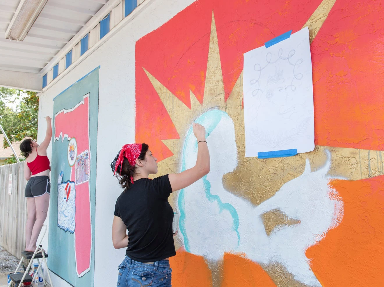University of West Florida students Whitney Hayek (right) and Kaylie Shultz paint murals on the exterior of the Shoreline Foods International Market & Deli in Pensacola on Thursday.