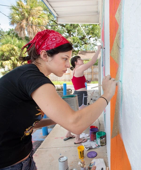 University of West Florida students Whitney Hayek, left, and Kaylie Shultz paint murals on the exterior of the Shoreline Foods International Market & Deli in Pensacola on Thursday.